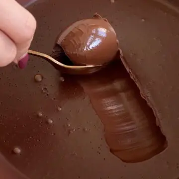 A hand held spoon takes a scoop from the top of a plant-based vegan chocolate ganache dessert